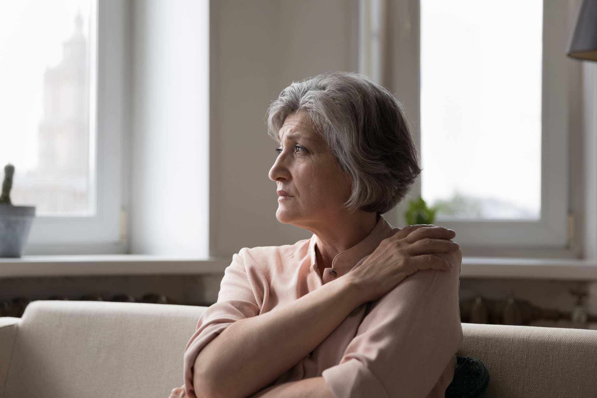 Older lady going through divorce sat on a chair looking sad and staring into space.