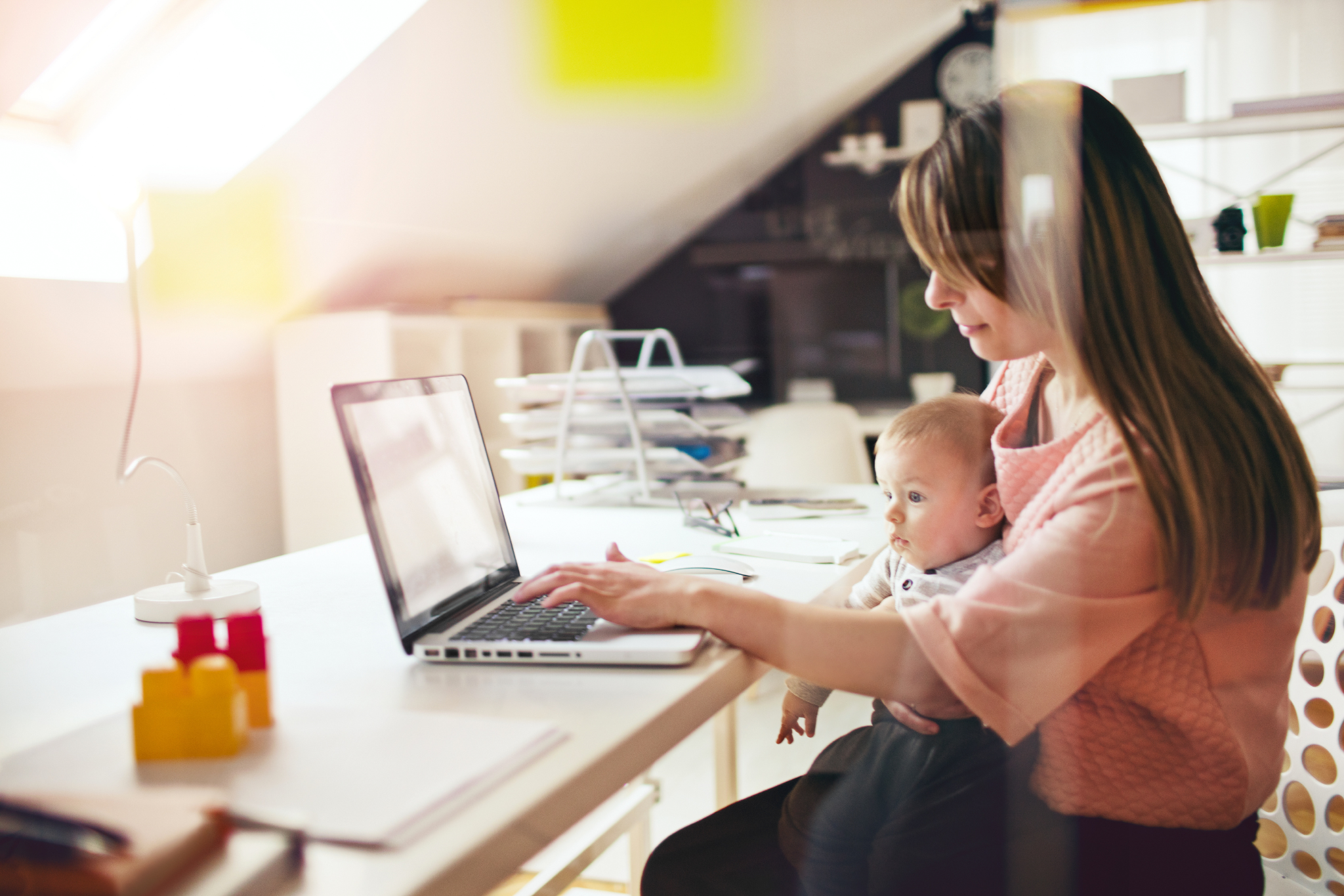 New mum sat at laptop with her baby, during a KIT day at work.