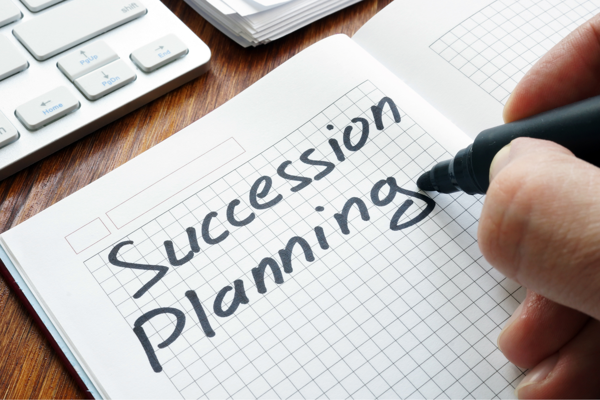 A hand writing Succession Planning in black marker pen on a notepad.
